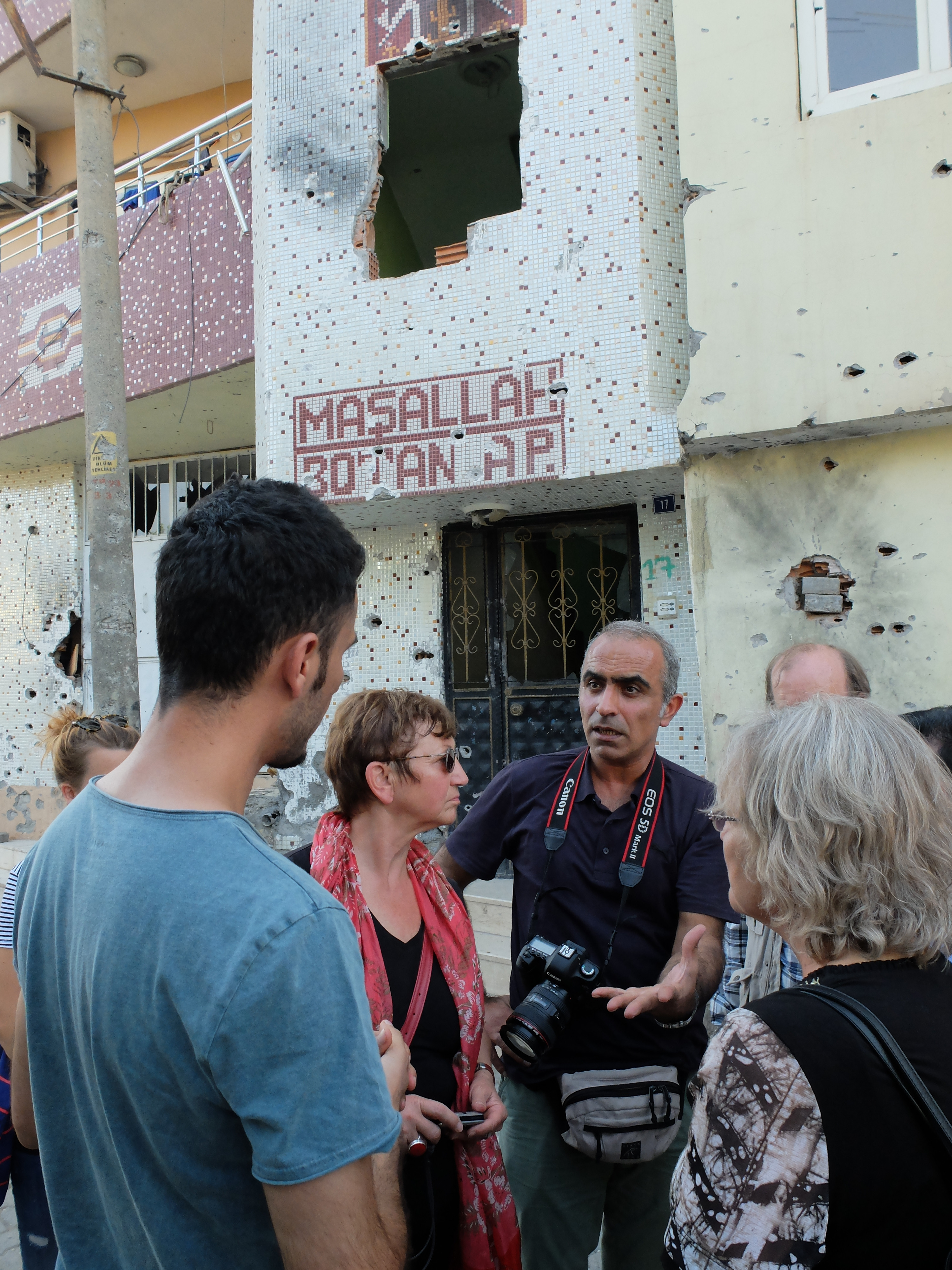 Heyet üyeleri Cizre'de top mermisiyle vurulmuş bir binanın önünde sokağa çıkma yasağı süresinde yaşananları dinliyor