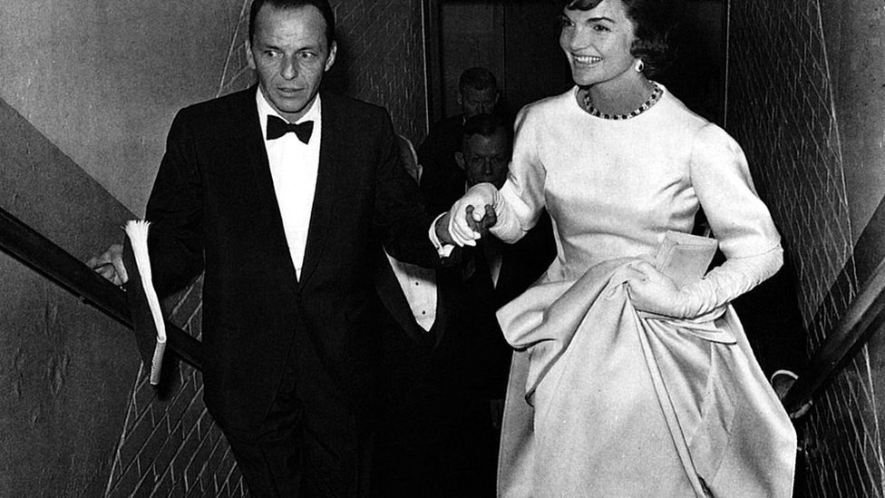 
                    John F Kennedy'nin yemin töreninin öncesindeki akşam bir galada çekilen bu fotoğrafta, Jacqueline Kennedy'ye sanatçı Frank Sinatra eşlik ediyor. Gala, Kennedy ve Demokrat Parti'nin kampanya harcamalarının karşılanması için düzenlenmişti.
                